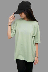 Person wearing a light green oversized shirt and black cap against a wooden background