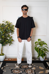 Man wearing a black t-shirt and white pants standing in a room with plants.