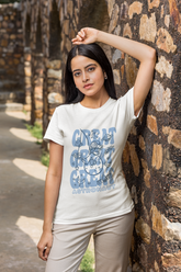 Woman wearing a white t-shirt with blue text and graphics, leaning against a stone wall.