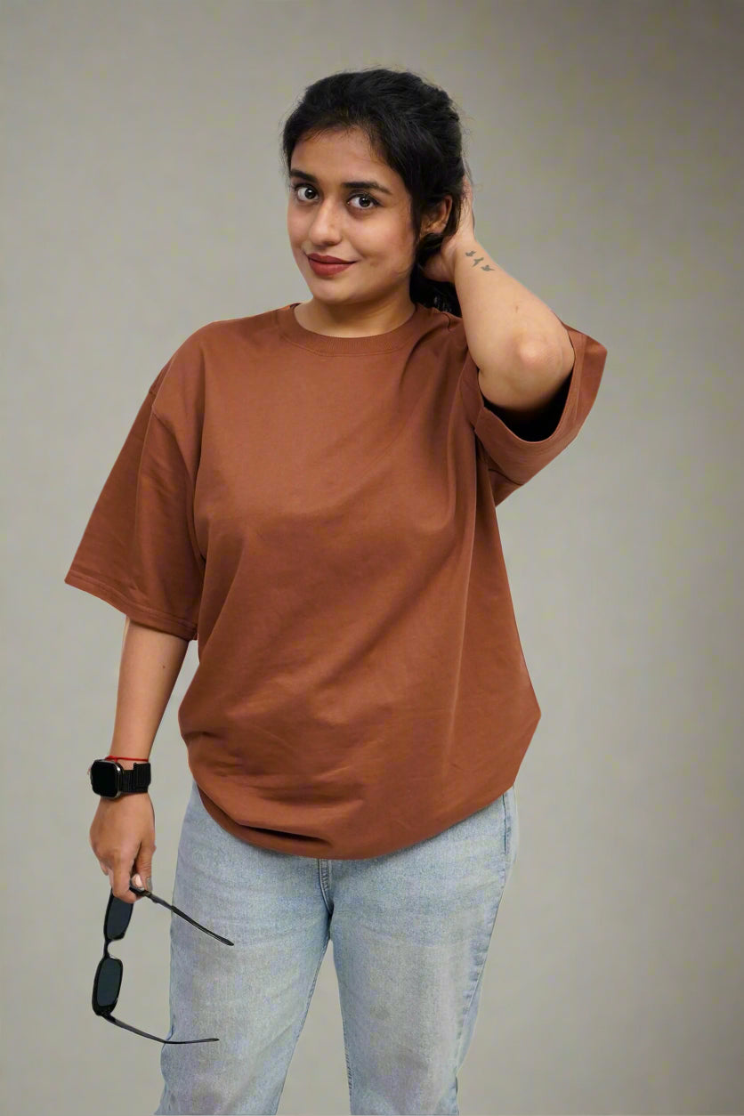 Person wearing a brown oversized shirt and light blue jeans against a white textured background