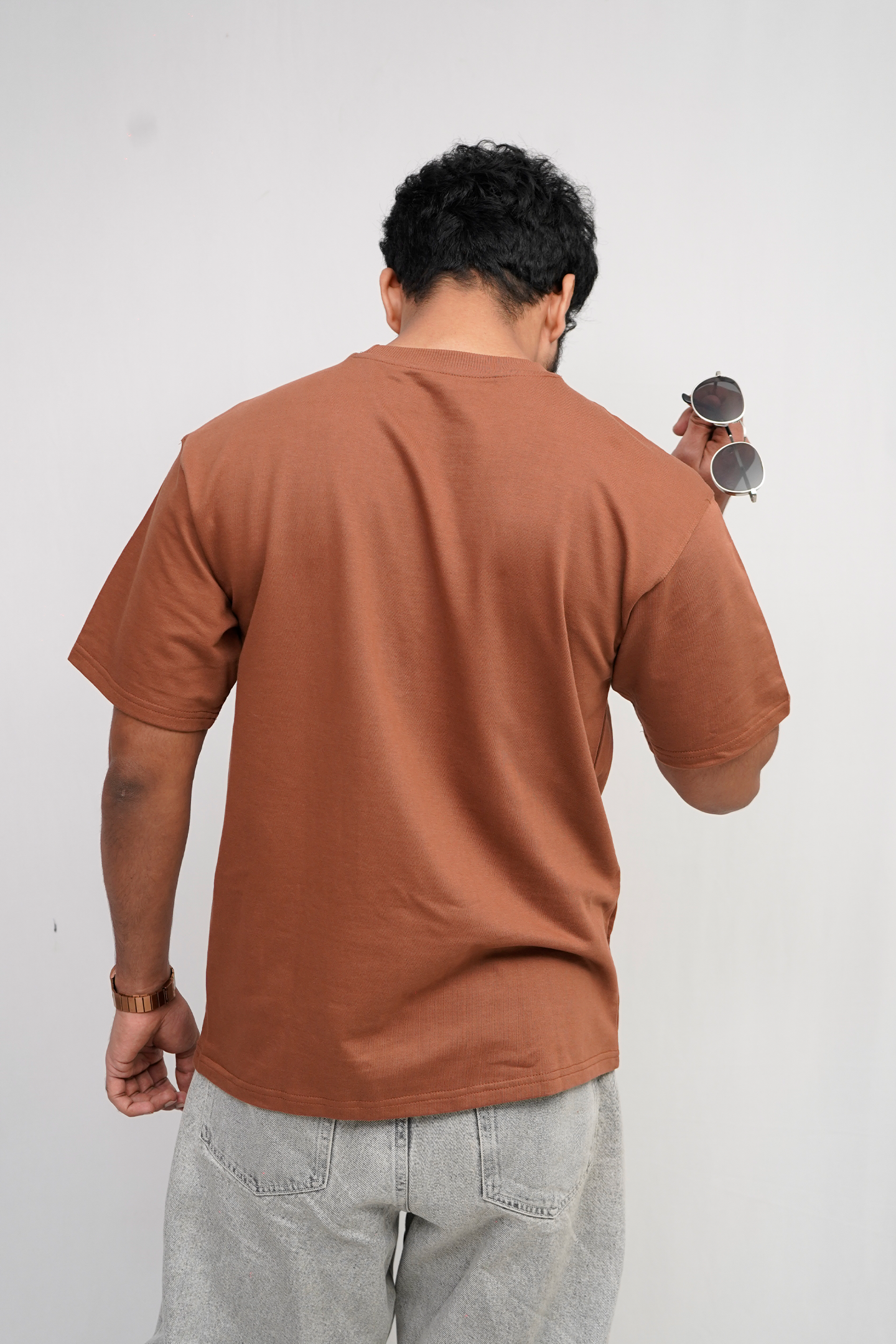 Person wearing a brown t-shirt and gray pants against a white background