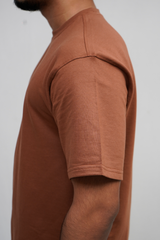 Person wearing a brown t-shirt against a plain background