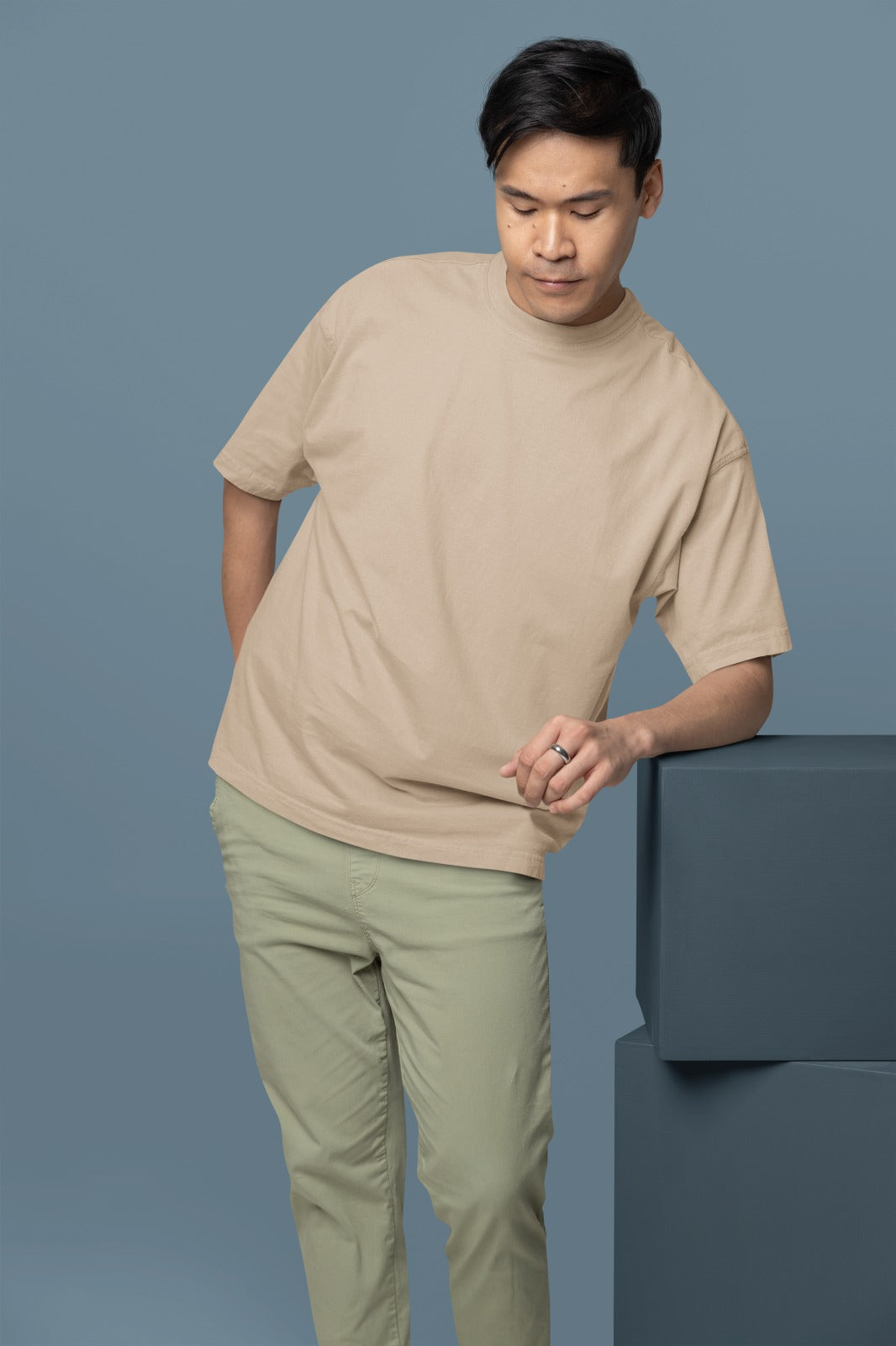 Man wearing a beige t-shirt and light green pants against a blue background
