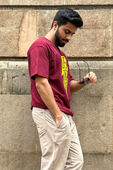 Man wearing a maroon t-shirt with yellow text against a stone wall.