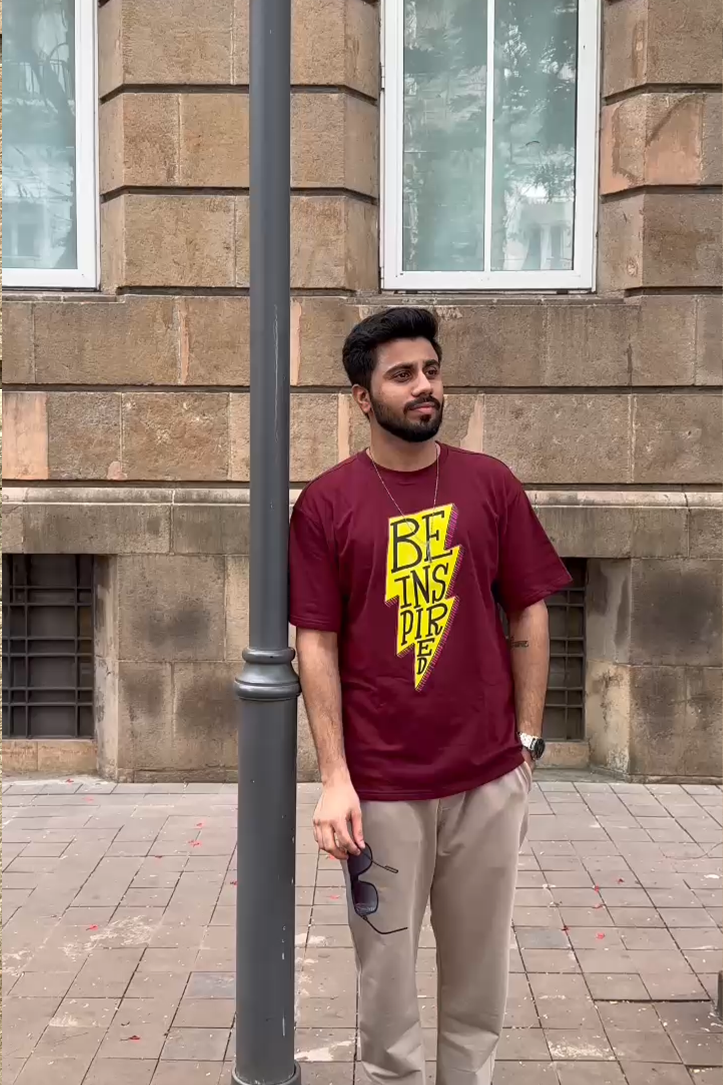 Man wearing a maroon t-shirt with yellow text standing against a brick wall.