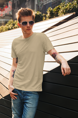 Man wearing sunglasses and a beige t-shirt leaning against a wooden wall.