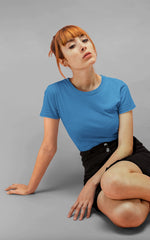Person wearing a blue t-shirt and black skirt sitting on a gray background
