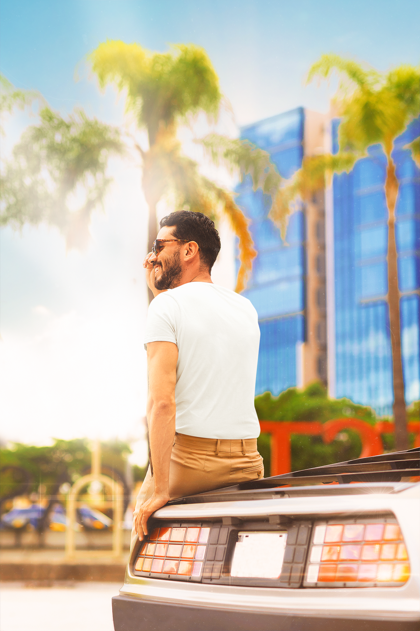 Man sitting on a car with palm trees and a building in the background Slim Fit T-Shirt From Kapda Kulture.