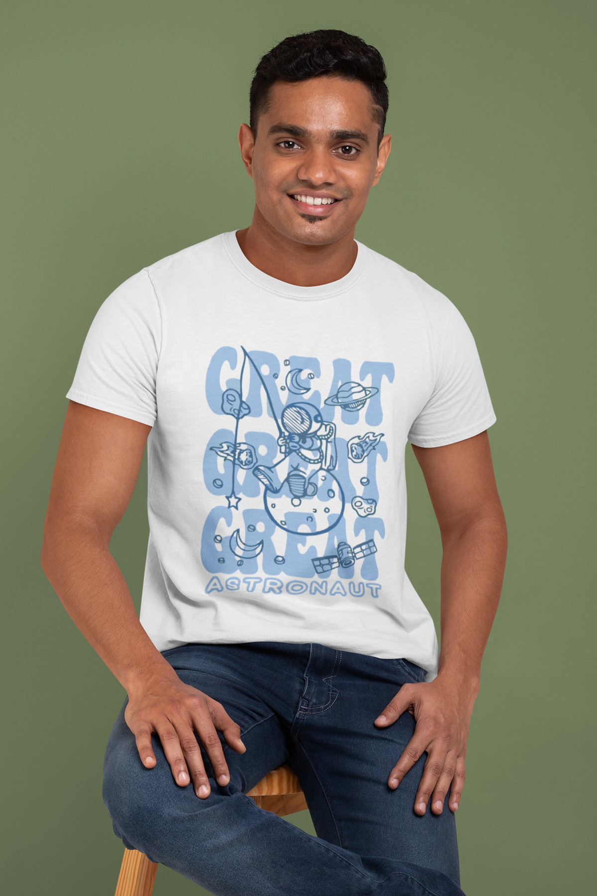 Man wearing a white t-shirt with blue graphics and text, sitting on a stool against a green background