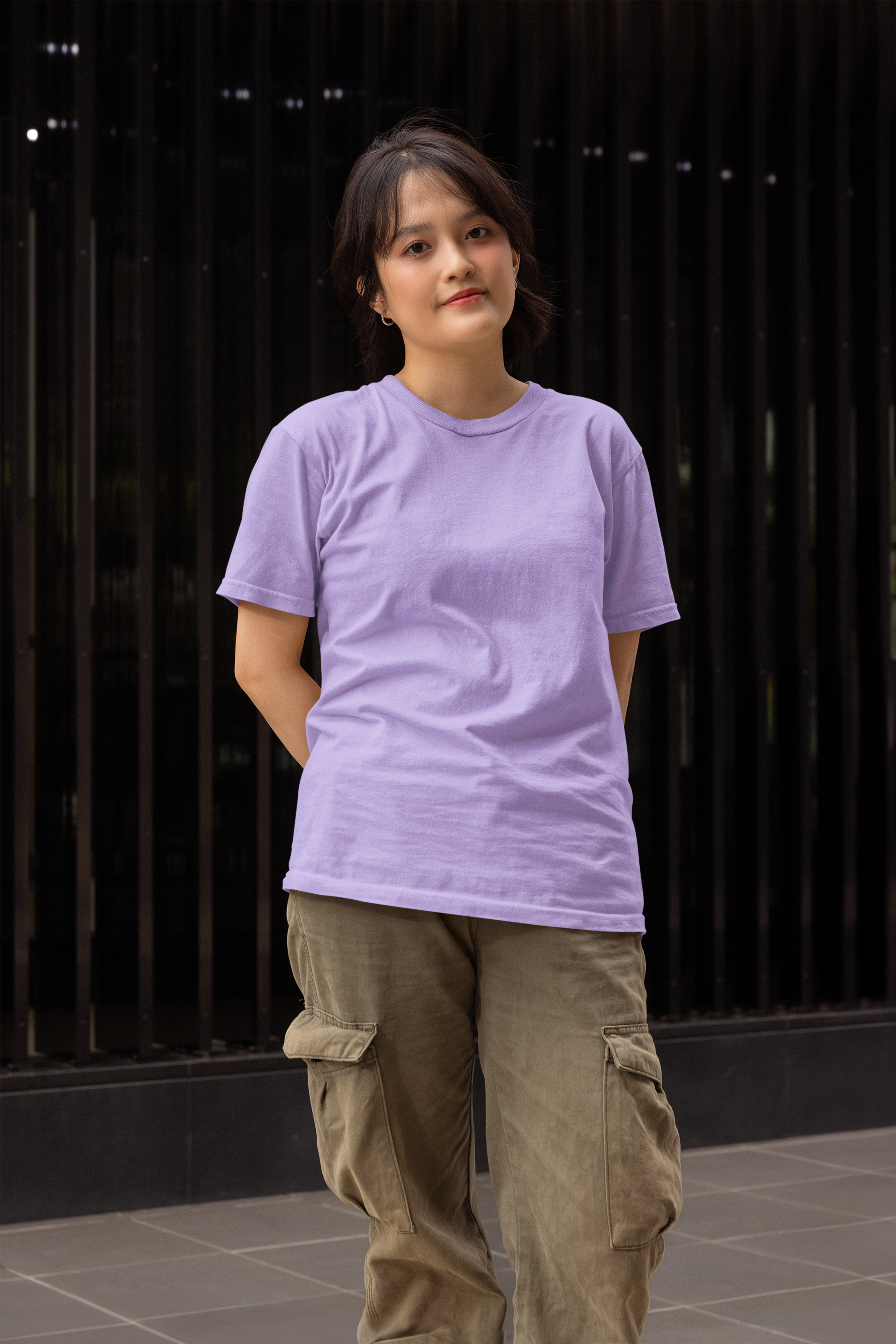 Person wearing a purple t-shirt and brown pants standing against a dark background