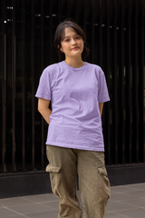 Person wearing a purple t-shirt and brown pants standing against a dark background