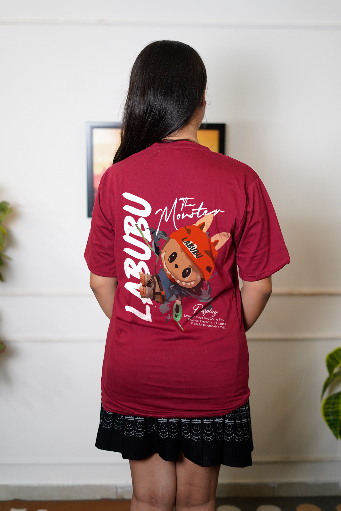 Person wearing a red t-shirt with a teddy bear graphic and text, standing indoors.