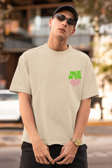 Man wearing a beige t-shirt with green text and black pants, standing outdoors  Oversized T-Shirt From Kapda Kulture.