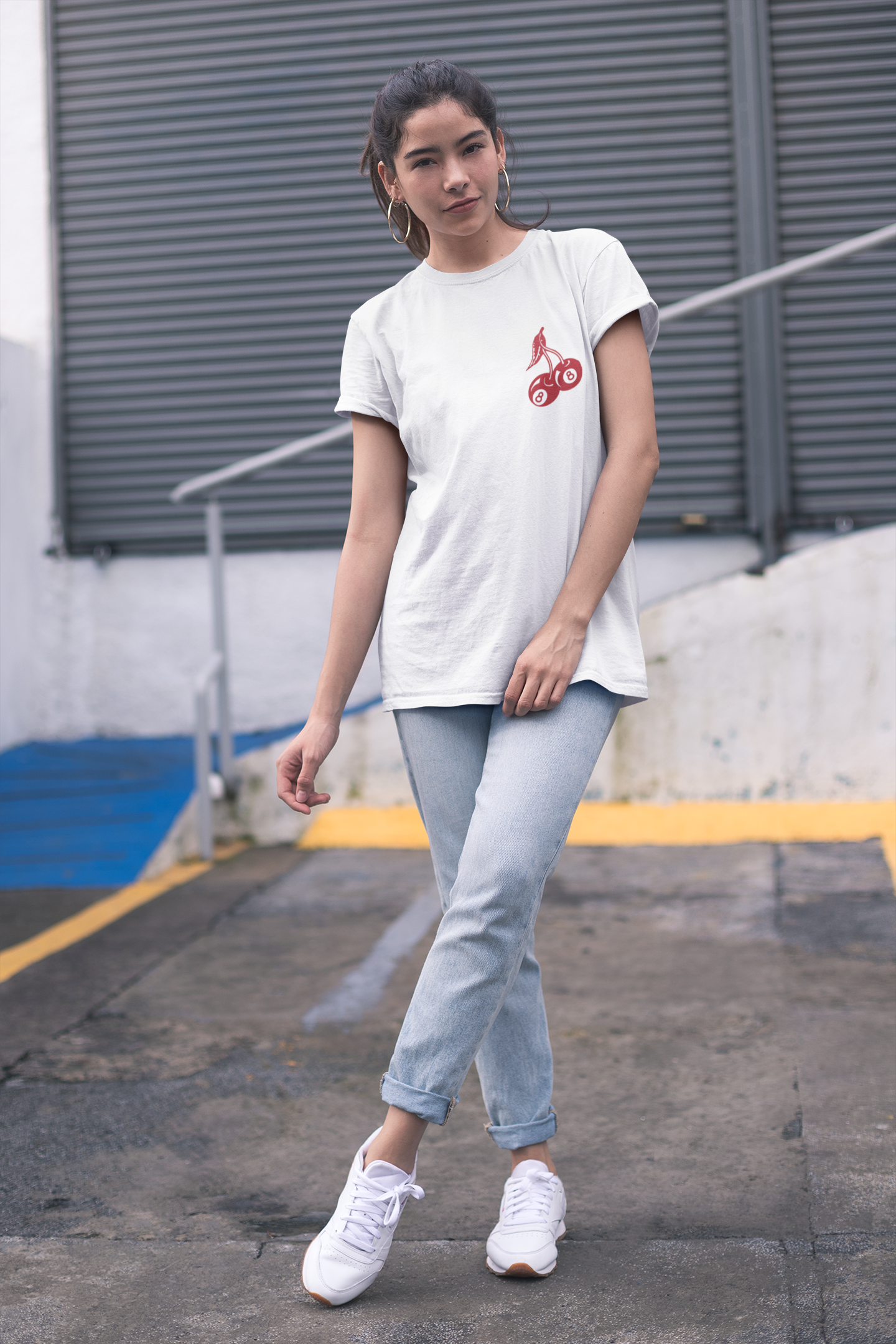 A woman wearing a white t-shirt with a graphic on the front, light blue jeans, and white sneakers.