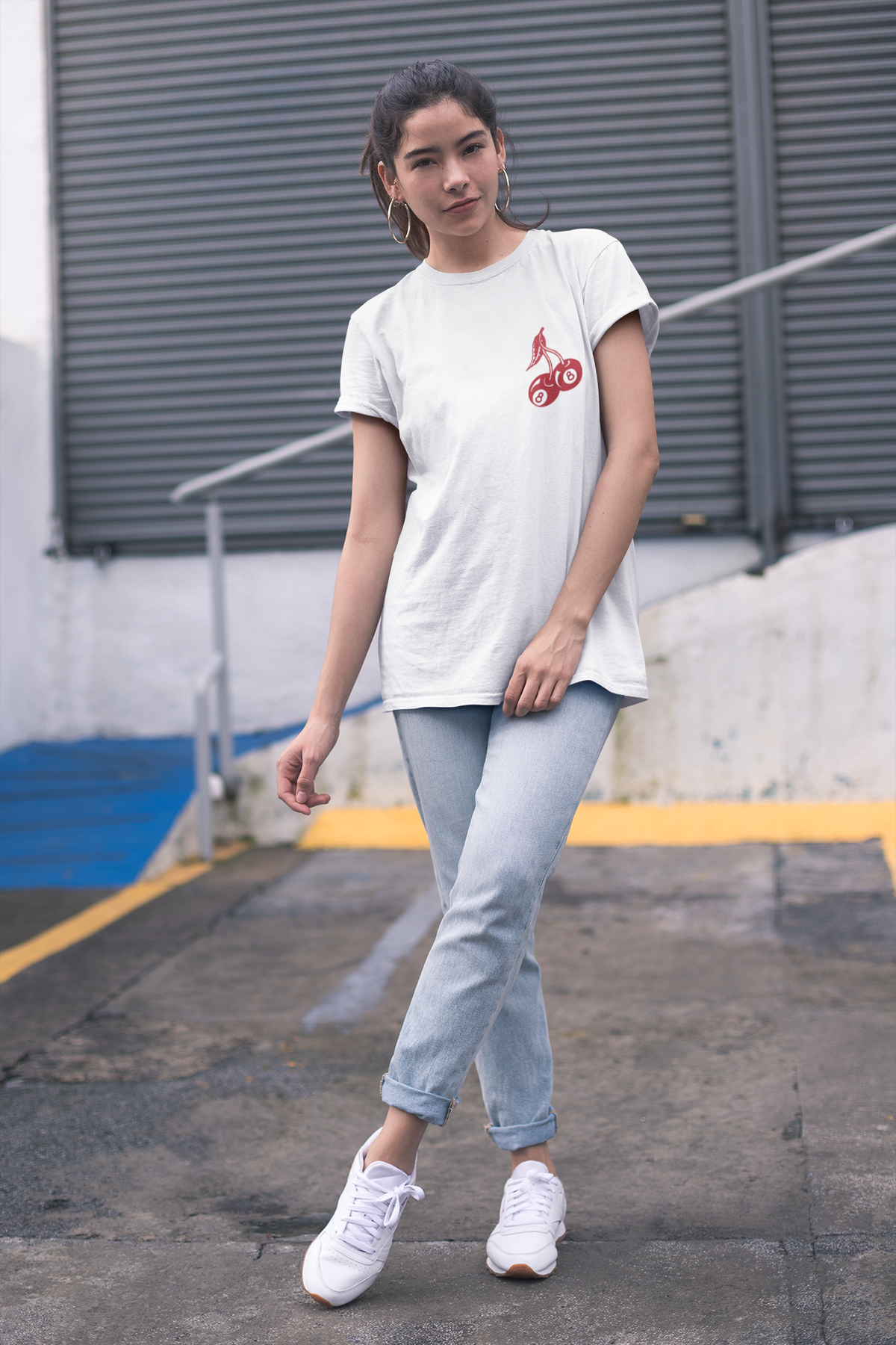 A woman wearing a white t-shirt with a graphic on the front, light blue jeans, and white sneakers.