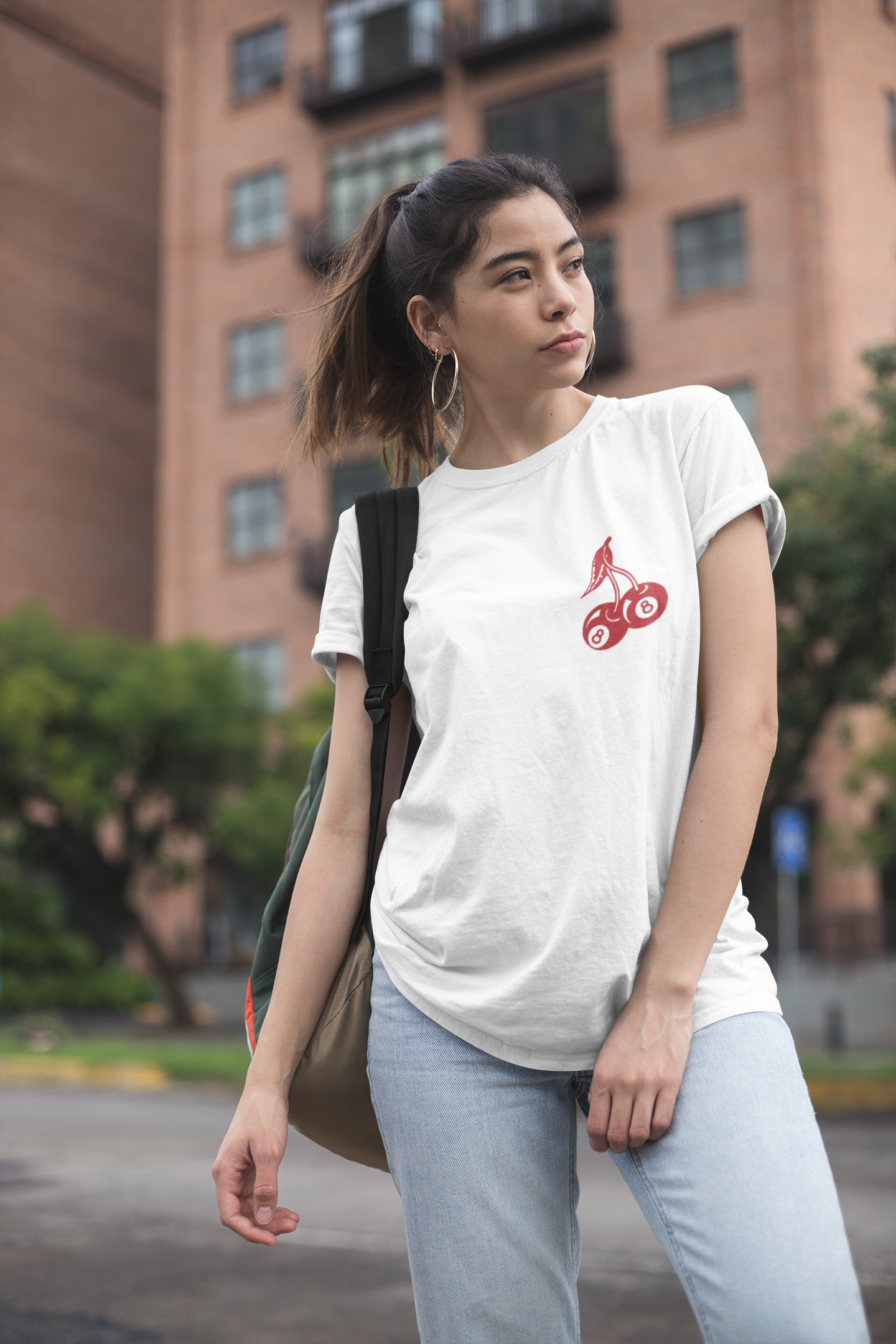 Woman wearing a white t-shirt with a red logo, walking in an urban environment.